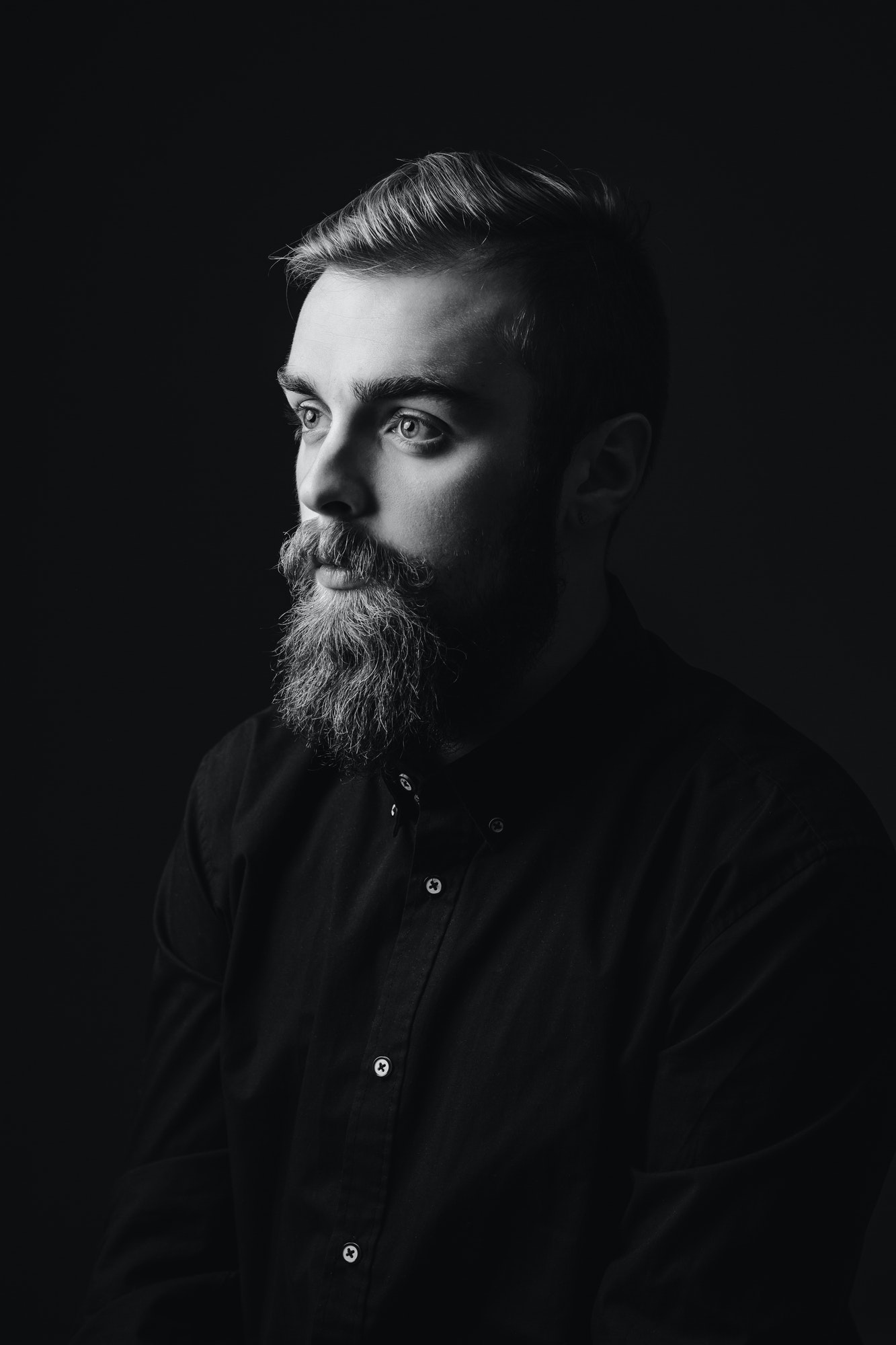 Black and white portrait of a stylish man with a beard and stylish hairdo dressed in the black shirt